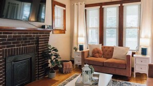 Una sala de estar con chimenea, un sofá, dos mesitas de noche con lámparas y un televisor montado en la pared.