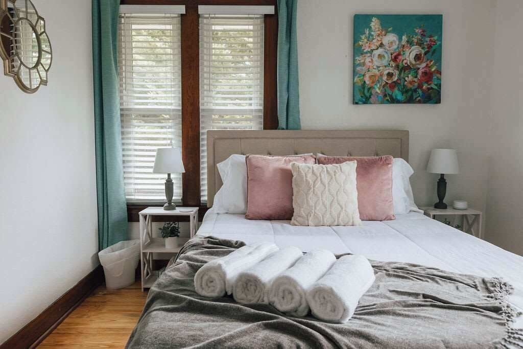 A neatly made bed with rolled towels, a bedside lamp, and a painting on the wall.