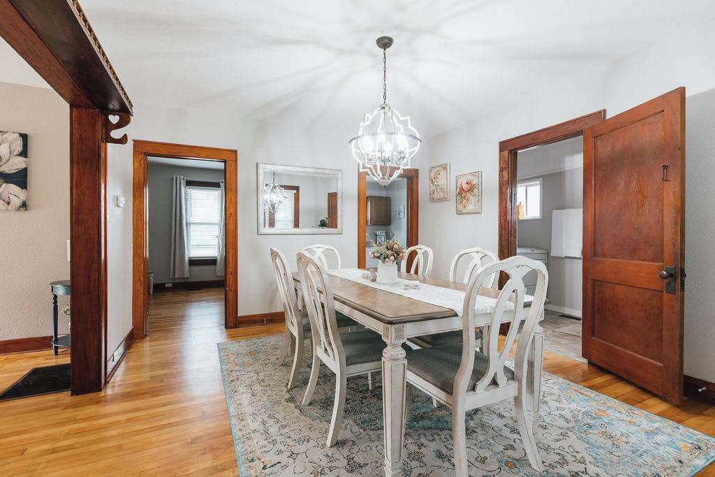 A dining room with a wooden table and chairs, a chandelier, and a patterned rug.