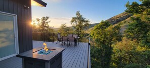 A deck with a fire feature, outdoor furniture, and a scenic view of hills and trees.