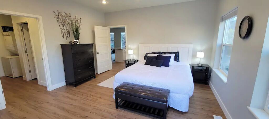 A bedroom with a large bed, a dresser, a bench, and a nightstand with a lamp.
