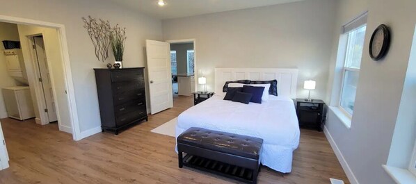 A bedroom with a large bed, a dresser, a bench, and a nightstand with a lamp.