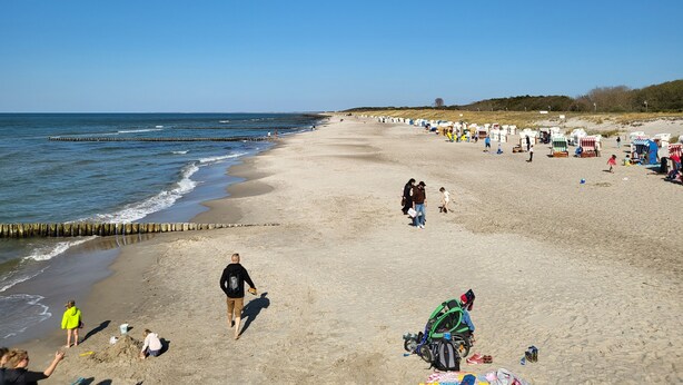 A wide sandy beach with a clear sky, a calm sea, and a row of beach huts on the right. - Cozy vacation apartment in the countryside with garden and terrace (Gelbensande)