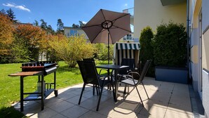An outdoor patio with a table and chairs, a large umbrella, and a small striped awning. - Cozy vacation apartment in the countryside with garden and terrace (Gelbensande)