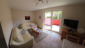 A living room with a sofa, a coffee table, a TV, and a sliding glass door leading to an outdoor area. - Cozy vacation apartment in the countryside with garden and terrace (Gelbensande)