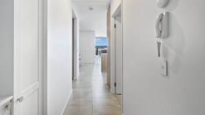 Un couloir aux murs blancs et au sol carrelé, qui mène à une pièce offrant une vue dégagée.