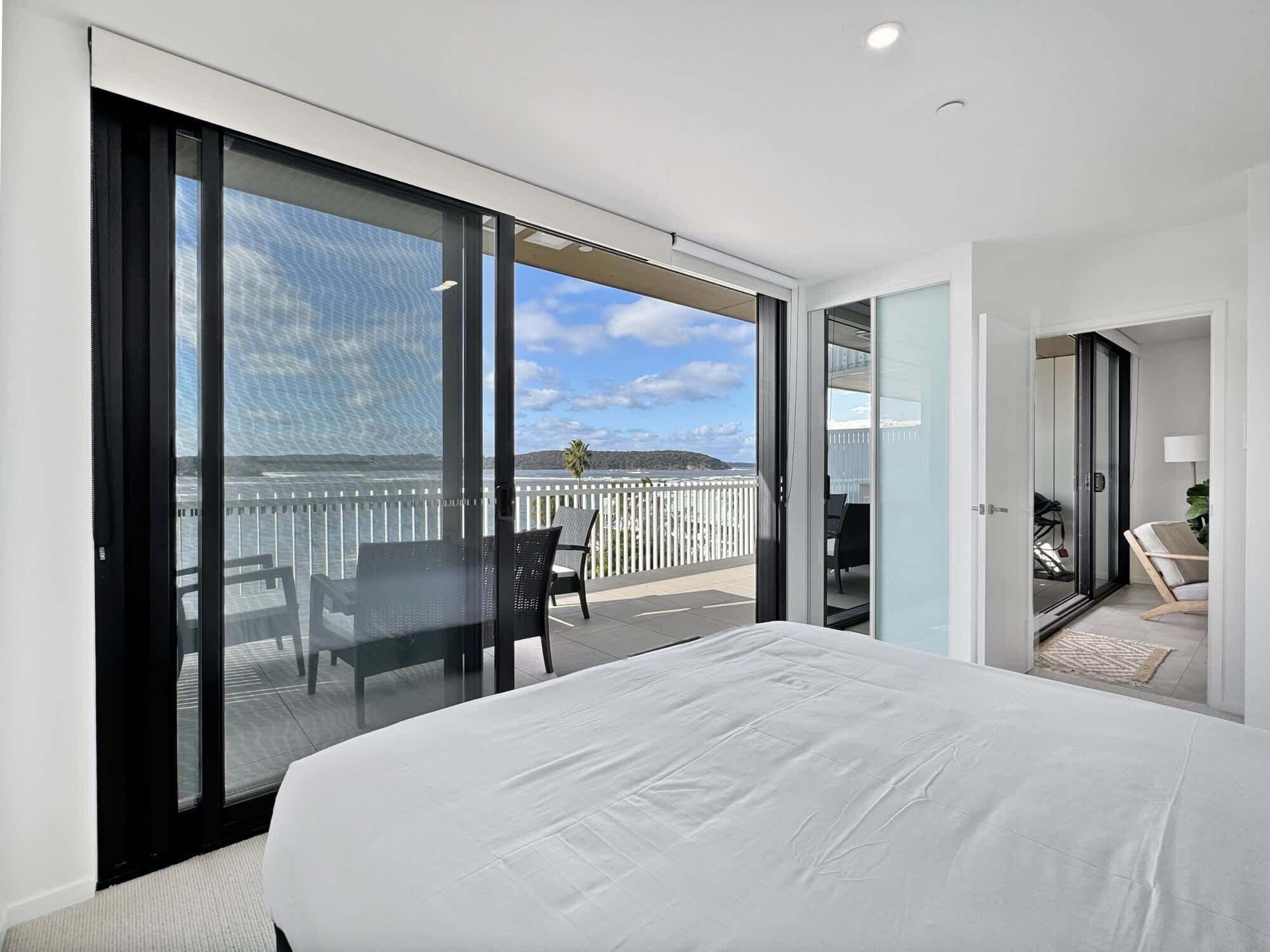 Ein modernes Hotelzimmer mit einem großen Bett, einem Balkon mit Meerblick und einer separaten Sitzecke mit Sessel und Tisch.