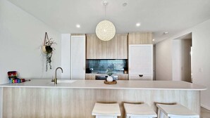 Une cuisine moderne dotée d’un îlot central, de tabourets de bar blancs et d’un luminaire suspendu.