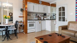 A modern kitchen with white cabinets, a dining area with a table and chairs, and a living room with a sofa. - On The Beach - Direct Beach Access, Sea Views (Saundersfoot)