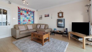 A living room with a beige sofa, wooden coffee table, and a flat-screen TV on a stand. - On The Beach - Direct Beach Access, Sea Views (Saundersfoot)