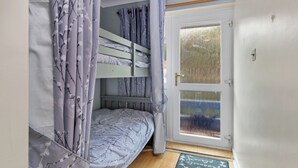 A room with a bunk bed, a door with a frosted glass panel, and a window with a view of trees. - On The Beach - Direct Beach Access, Sea Views (Saundersfoot)