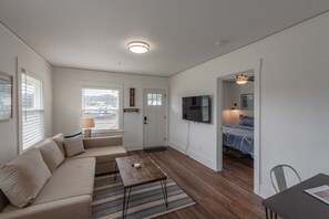 Cozy living space with a sofa, coffee table, and TV, featuring a comfortable bed in the background.