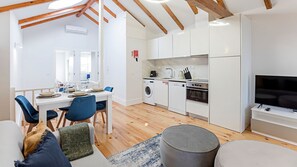 A compact kitchen with a washing machine, oven, and a TV.