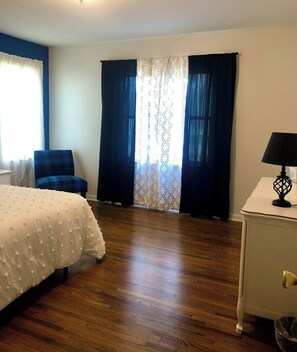 Une chambre d’hôtel avec un lit, une chaise, un bureau et une fenêtre avec des rideaux.
