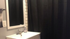 Un bagno con un lavandino bianco, uno specchio, un water e una tenda da doccia nera.