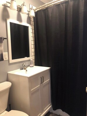Une salle de bain avec un lavabo blanc, un miroir, des toilettes et un rideau de douche noir.