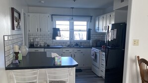 A kitchen with white cabinets, a black refrigerator, and two white bar stools.