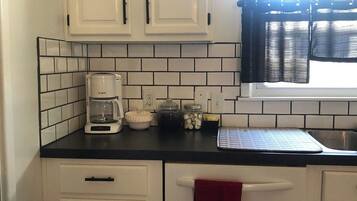 A kitchen with white cabinets, a coffee maker, a kettle, and a window with a curtain.