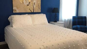 Ein Schlafzimmer mit einem großen Bett, einem Nachttisch, einer Lampe, einem Sessel und zwei Wandbildern.