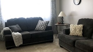 A living room with two dark sofas, a patterned throw blanket, a clock, and a lamp on a side table.