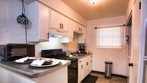 Una cocina compacta con armarios blancos, un microondas, una estufa y un cubo de basura.