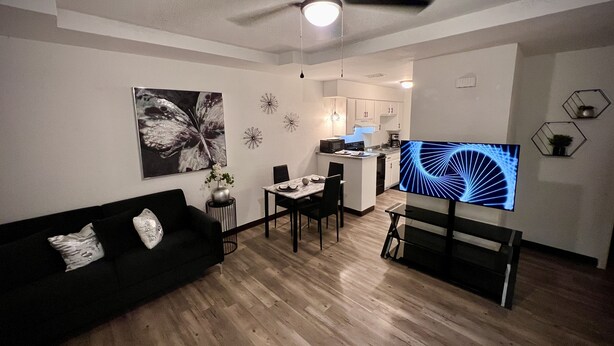 Una sala de estar moderna con un sofá negro, una mesa de comedor y un televisor.