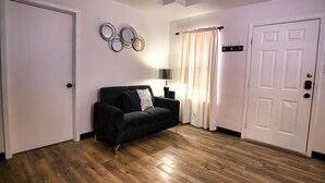 Una habitación con un sofá negro, una puerta blanca y suelo de madera.