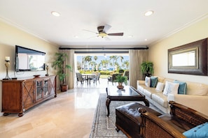 A spacious living room with a large window, a ceiling fan, a wooden cabinet, and a leather sofa.