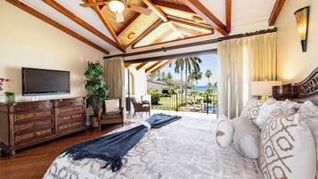 A spacious bedroom with a large bed, wooden ceiling beams, a television, and a view of the outdoors.