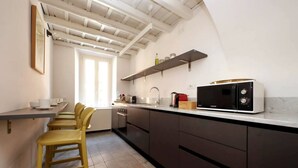 Une cuisine moderne avec des meubles de couleur sombre, un plan de travail blanc, un four à micro-ondes et une fenêtre laissant entrer la lumière naturelle.