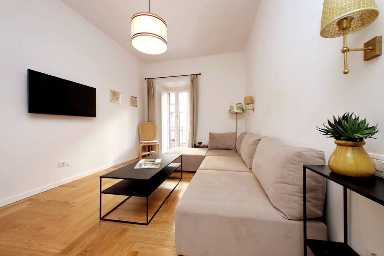 Una sala de estar moderna con un sofá, una mesa de centro, un televisor montado en la pared y una lámpara.