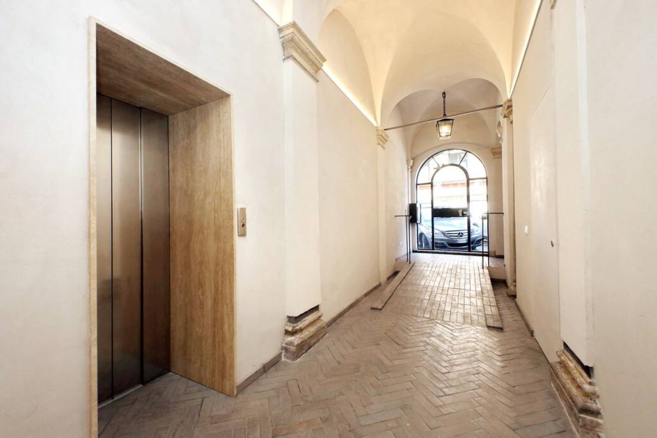 A hallway with a wooden elevator, white walls, and a herringbone floor pattern.