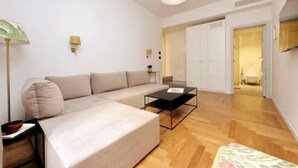 Un salon moderne avec un canapé, une table basse et une lampe. Une porte donne accès à une autre pièce.