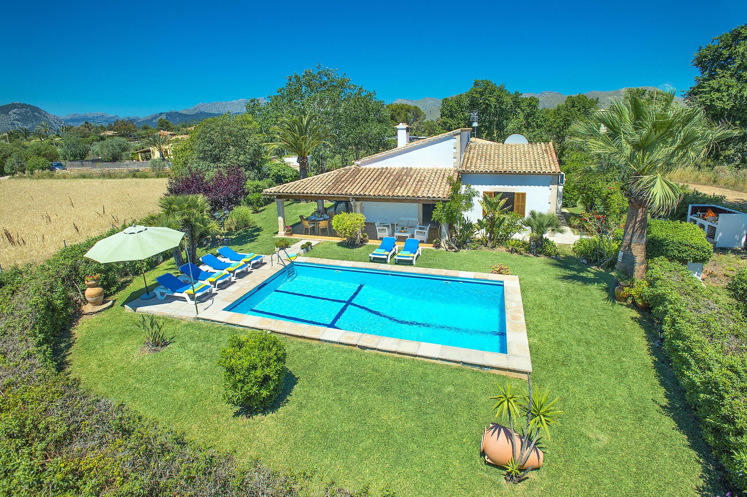 Una casa con piscina, rodeada de césped cuidado y palmeras.