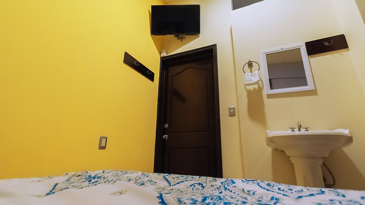Una habitación pequeña con una cama, una puerta, un lavamanos y un espejo.