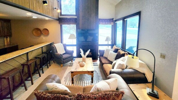 Una sala acogedora con chimenea, asientos cómodos y una cocina con taburetes de bar.