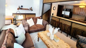 Una sala de estar acogedora con un sofá de cuero marrón, una mesa de centro de madera y una cocina a la vista.