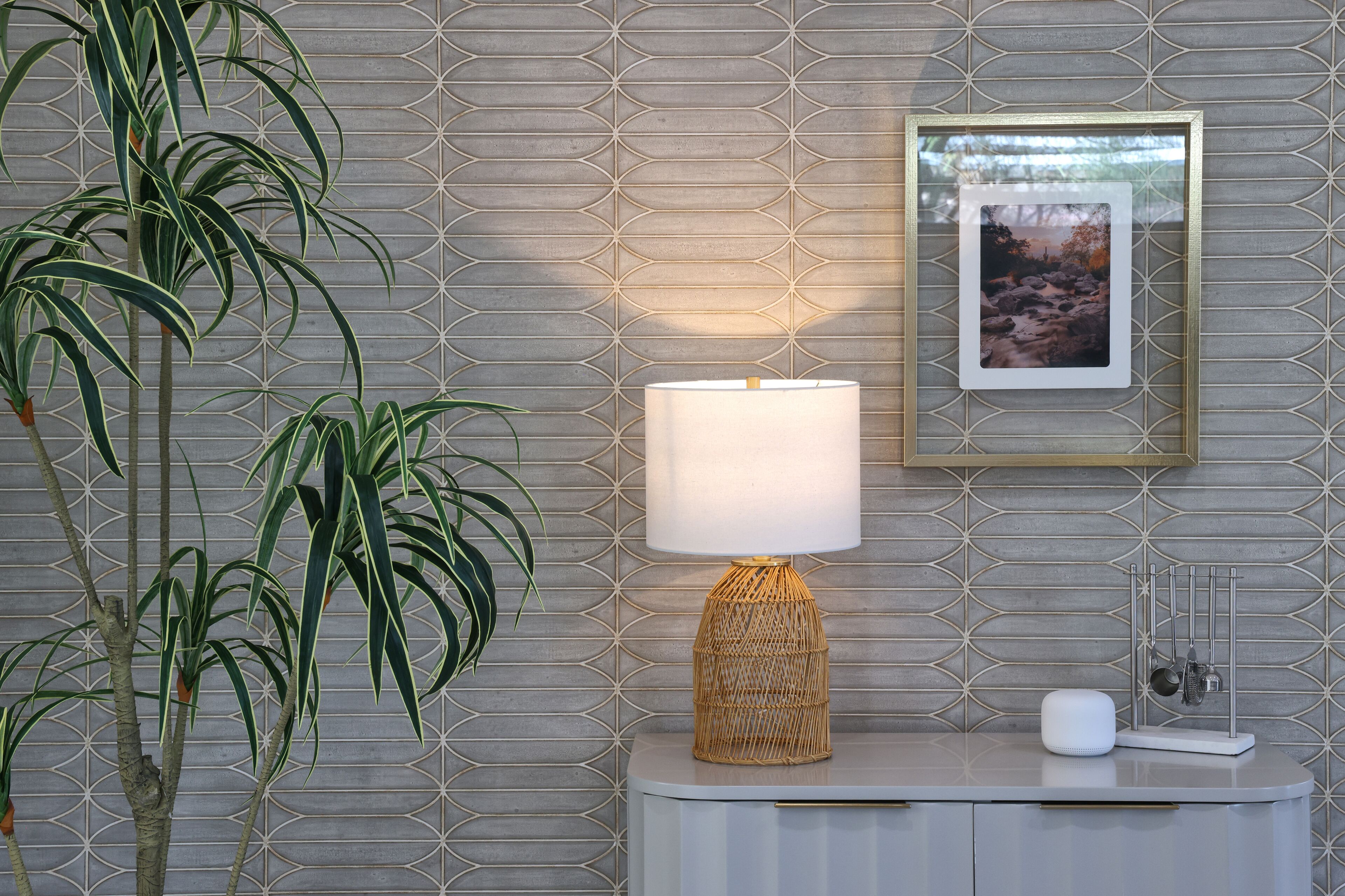A modern room with a geometric patterned wall, a standing lamp, a framed picture, and a plant.
