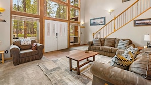 A spacious living room with large windows, a wooden staircase, and a cozy seating area.