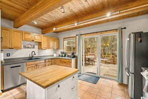 Una cucina con mobili in legno, lavastoviglie in acciaio inossidabile e una grande isola con piano di lavoro in legno.