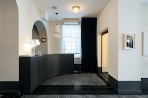 Un área de recepción moderna con un mostrador curvo, una lámpara de pared, una ventana con cortinas y obras de arte enmarcadas en la pared.