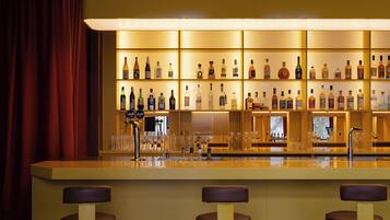 A bar area with a long counter, multiple stools, and shelves stocked with bottles.