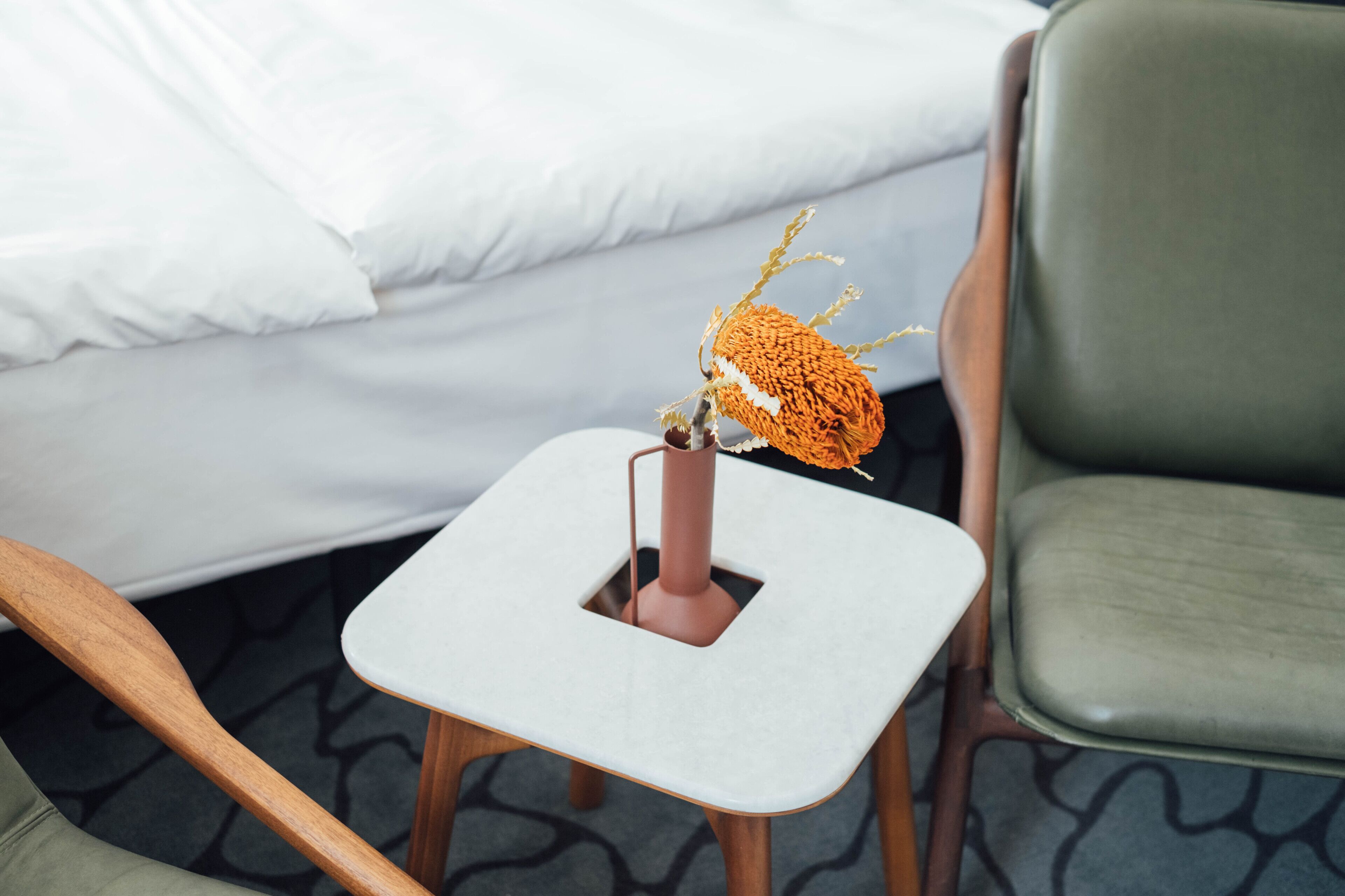 A small white table with a brown vase and a plant in a hotel room.