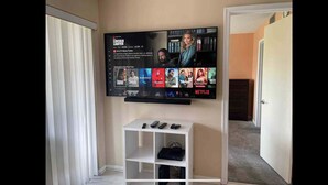 A flat-screen TV mounted on a wall with a Netflix interface displaying various shows. Below the TV, there is a white entertainment unit with electronic devices. - On the water and golf course view (St. Petersburg)