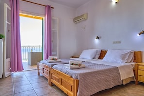 Quarto com duas camas, varanda com cortinas roxas, ar condicionado e uma pequena mesa de cabeceira.
