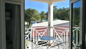 A covered outdoor area with a white railing, a small table, and a view of a building with a red roof. - Pomme Cannelle, un paisible T2Bis idéalement situé (Le Diamant)