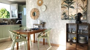 A kitchen with a wooden table, two chairs, a coffee maker, and a shelf with dishes and glasses. - Pomme Cannelle, un paisible T2Bis idéalement situé (Le Diamant)
