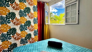 A room with a bed, a window with a view of greenery, and a patterned wall. - Pomme Cannelle, un paisible T2Bis idéalement situé (Le Diamant)