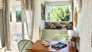 A cozy kitchen with a dining area, featuring a window with a view of trees, a sink, and a coffee maker. - Pomme Cannelle, un paisible T2Bis idéalement situé (Le Diamant)