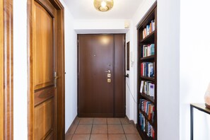 A hallway with a wooden door, a bookshelf, and a tiled floor.